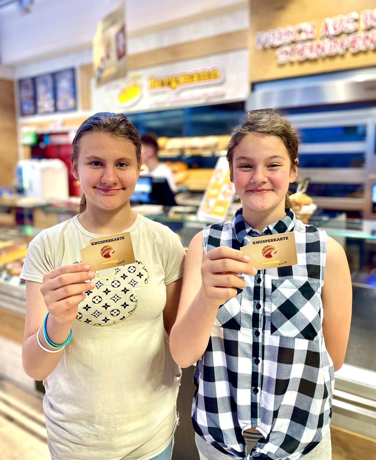 Leonie und Lucy halten lachend ihre Knusperkarten in einer Bäckerei Bergmann-Filiale