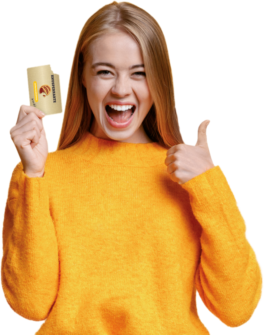 Junge Frau im orangen Pulli, lacht, hält die Knusperkarte hoch und zeigt Daumen hoch